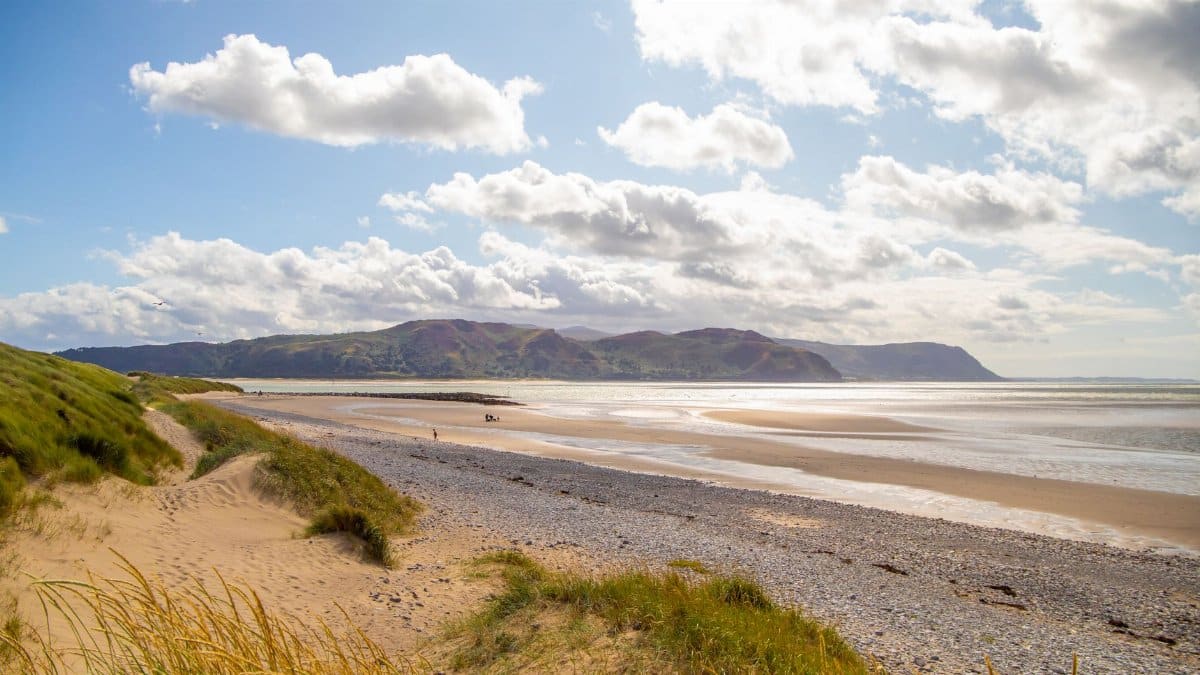 Sunlit beach with dunes and ocean at Llandudno, Wales, offering a serene coastal landscape.