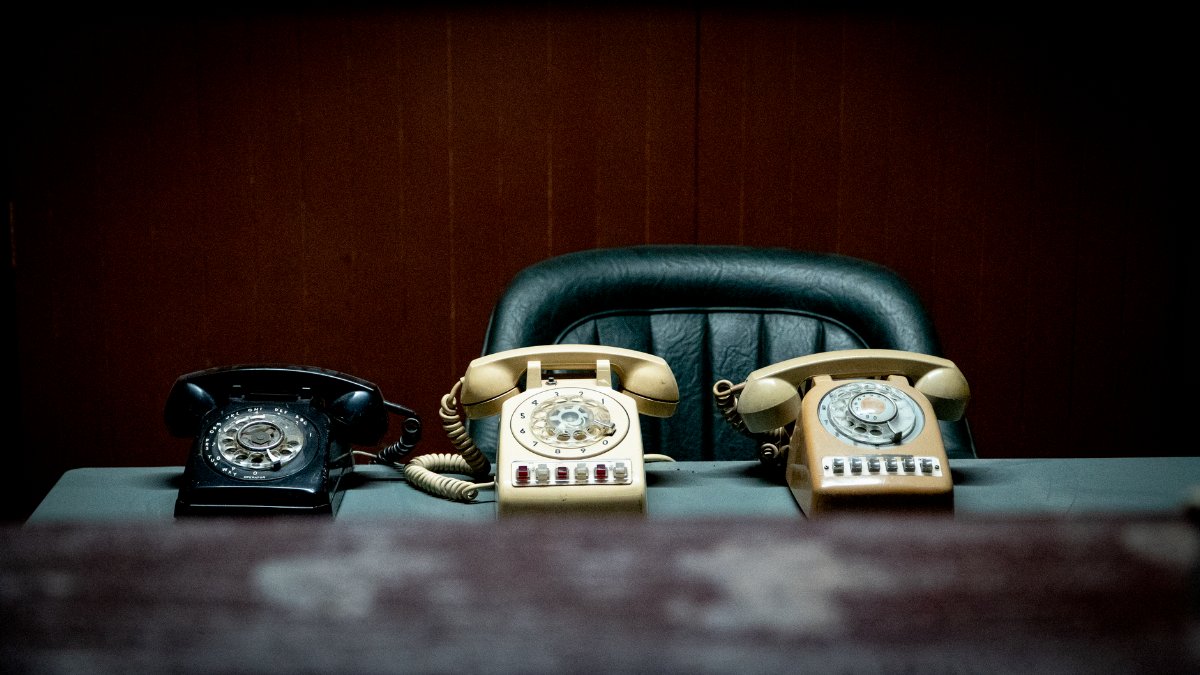 Three vintage rotary phones on an empty desk evoke nostalgia and classic communication.