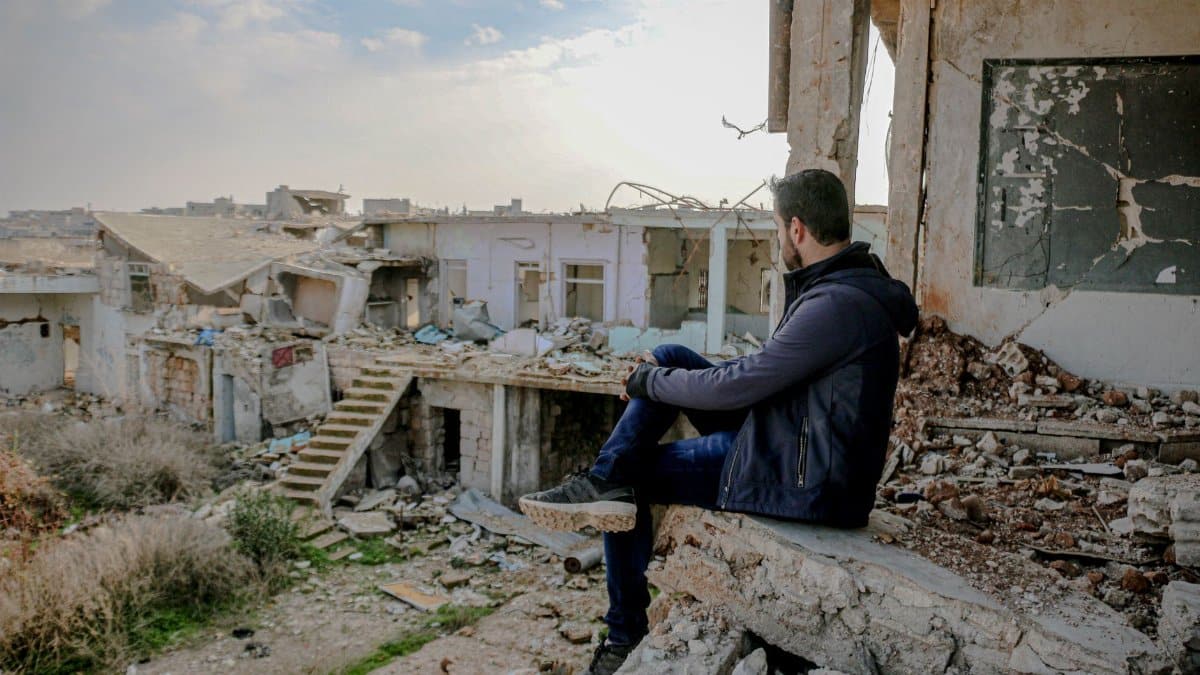 Side view of anonymous male sitting on concrete remains of broken house in desolated poor district with neglected buildings on street