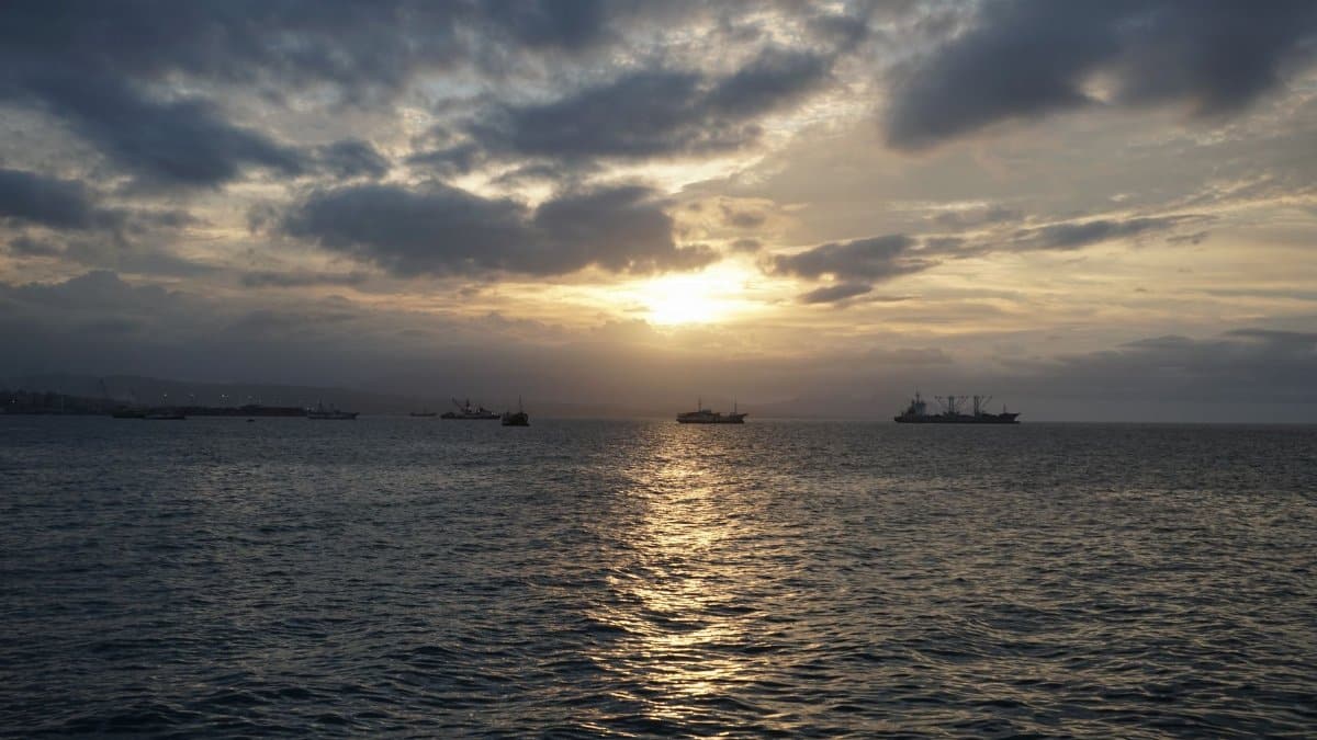 A serene sunset over the sea in the Solomon Islands with silhouetted ships on the horizon.
