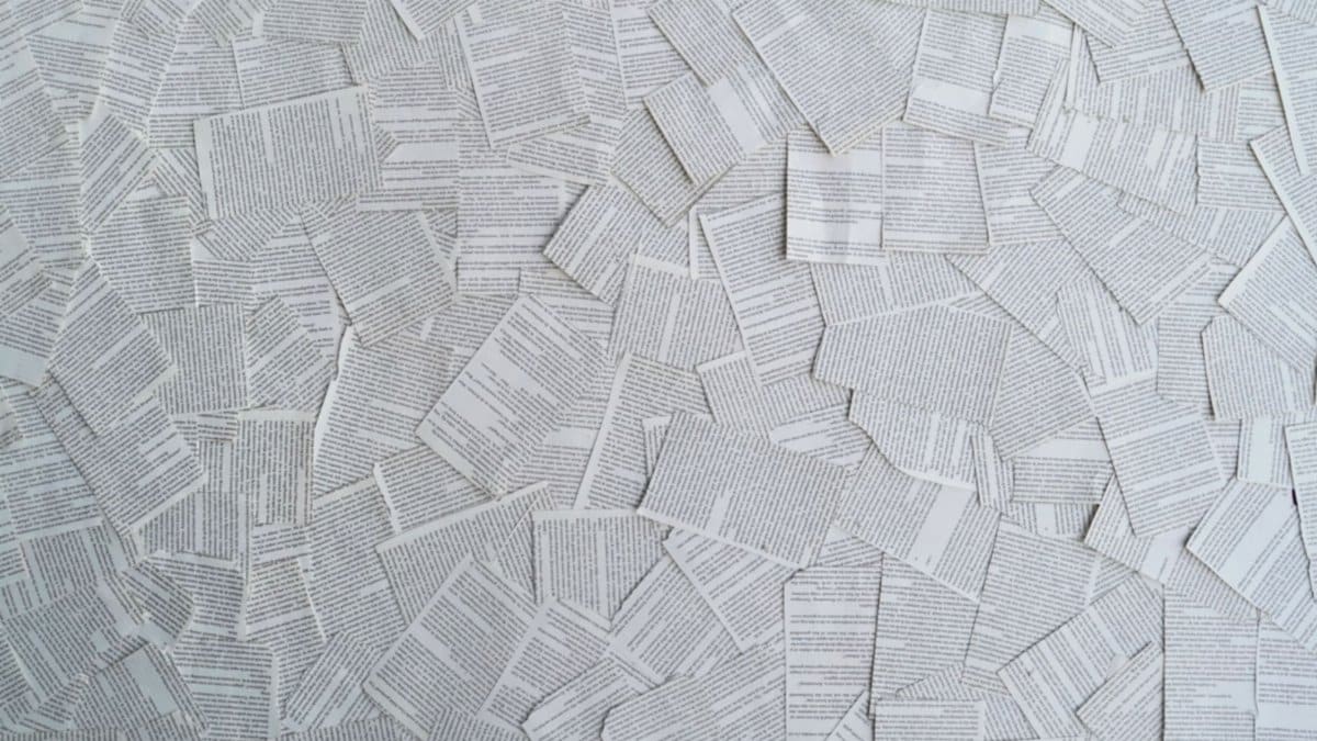 A top view of white and gray text-heavy book pages scattered randomly, creating a textured pattern.