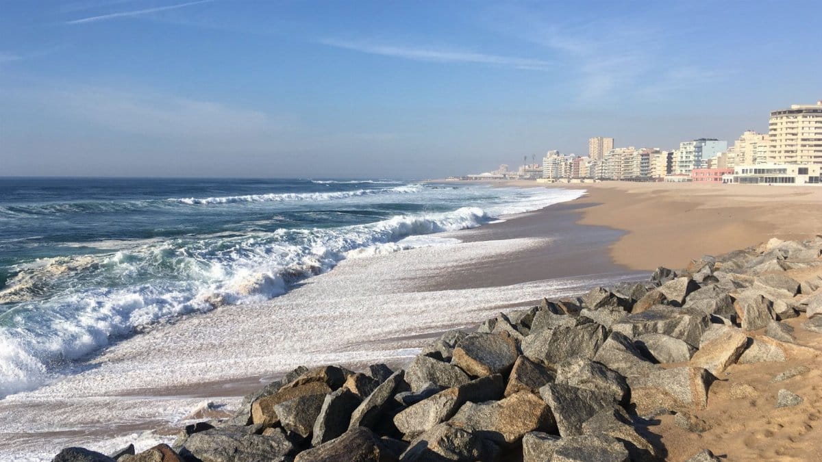 Waves crashing on the sandy beach of Espinho, Portugal on a sunny day with a city backdrop.