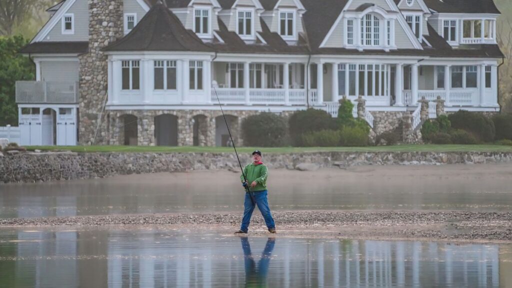 Serene scene of a man fishing in front of a grand lakeside mansion.