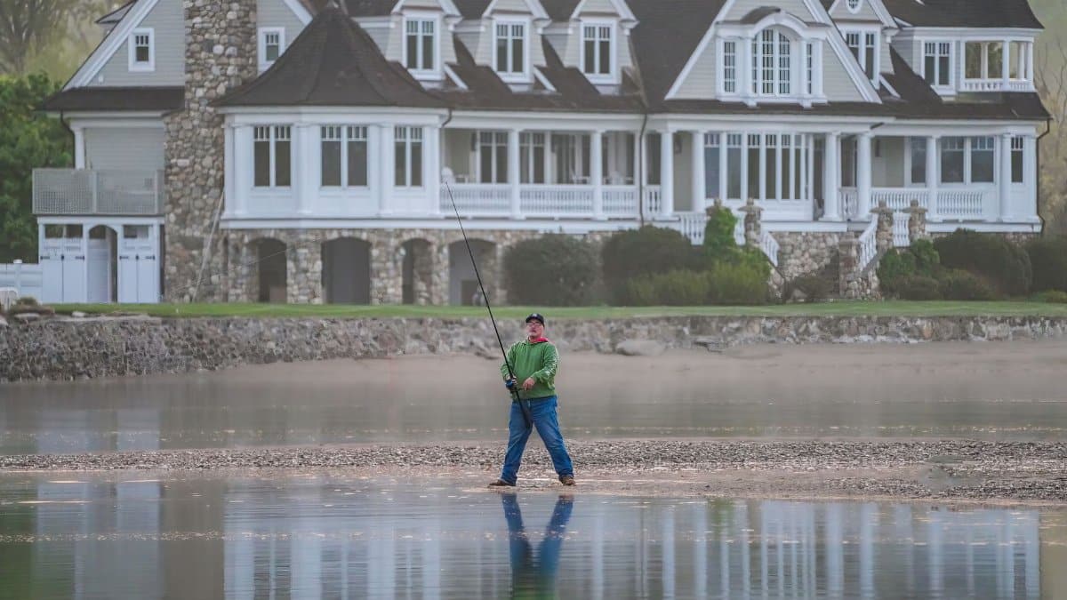 Serene scene of a man fishing in front of a grand lakeside mansion.
