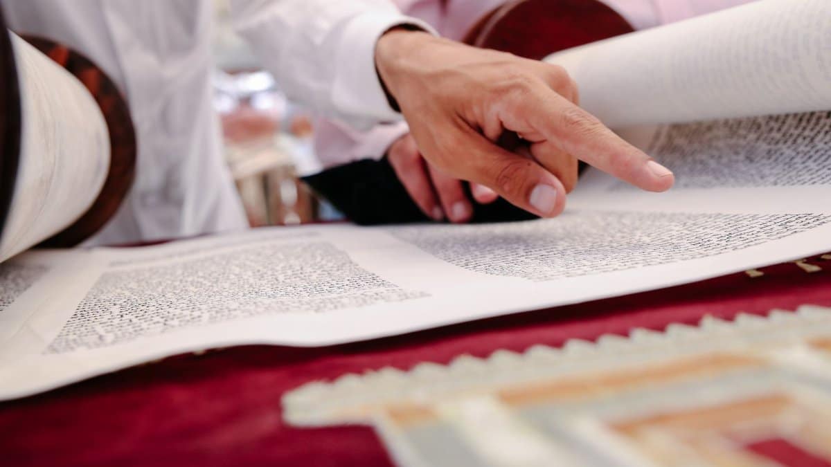 Hands pointing to text in a Torah scroll, symbolizing Jewish faith and traditions.