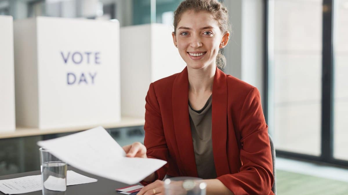 Cheerful young woman sitting indoors, holding documents during vote day with a smile.