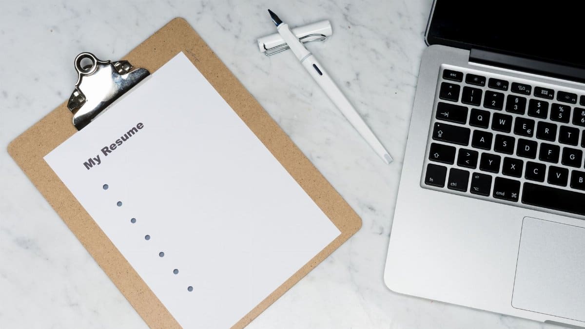 A clipboard with a resume beside a pen and laptop on a marble desk, ideal for business and job application themes.