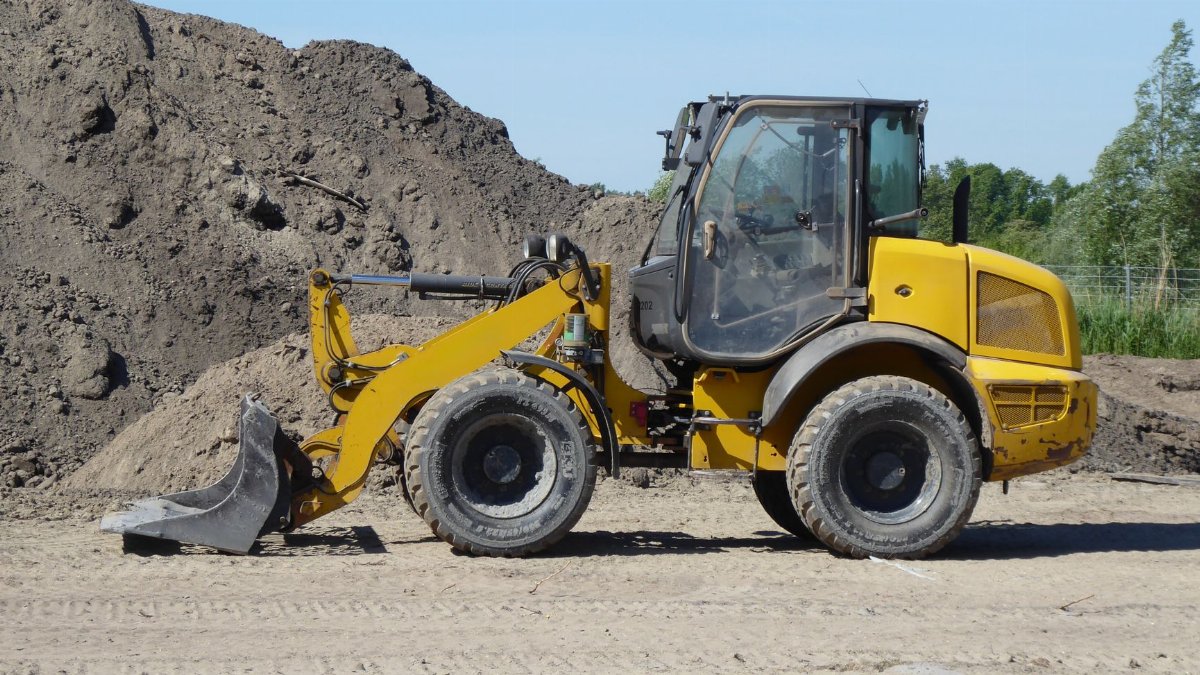 Side view of a yellow loader at a construction site with dirt mounds.