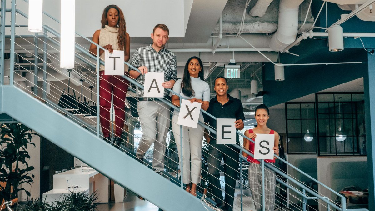 Multicultural business team holding 'Taxes' signs on a modern office staircase, symbolizing collaboration.