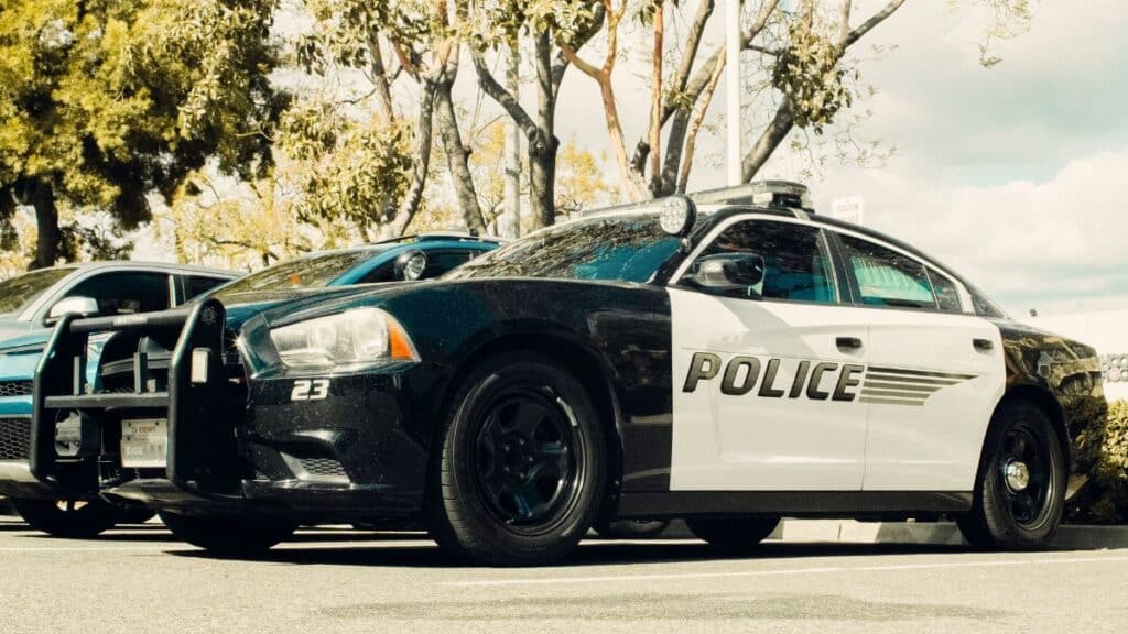Black and white police car parked outdoors with trees in the background.