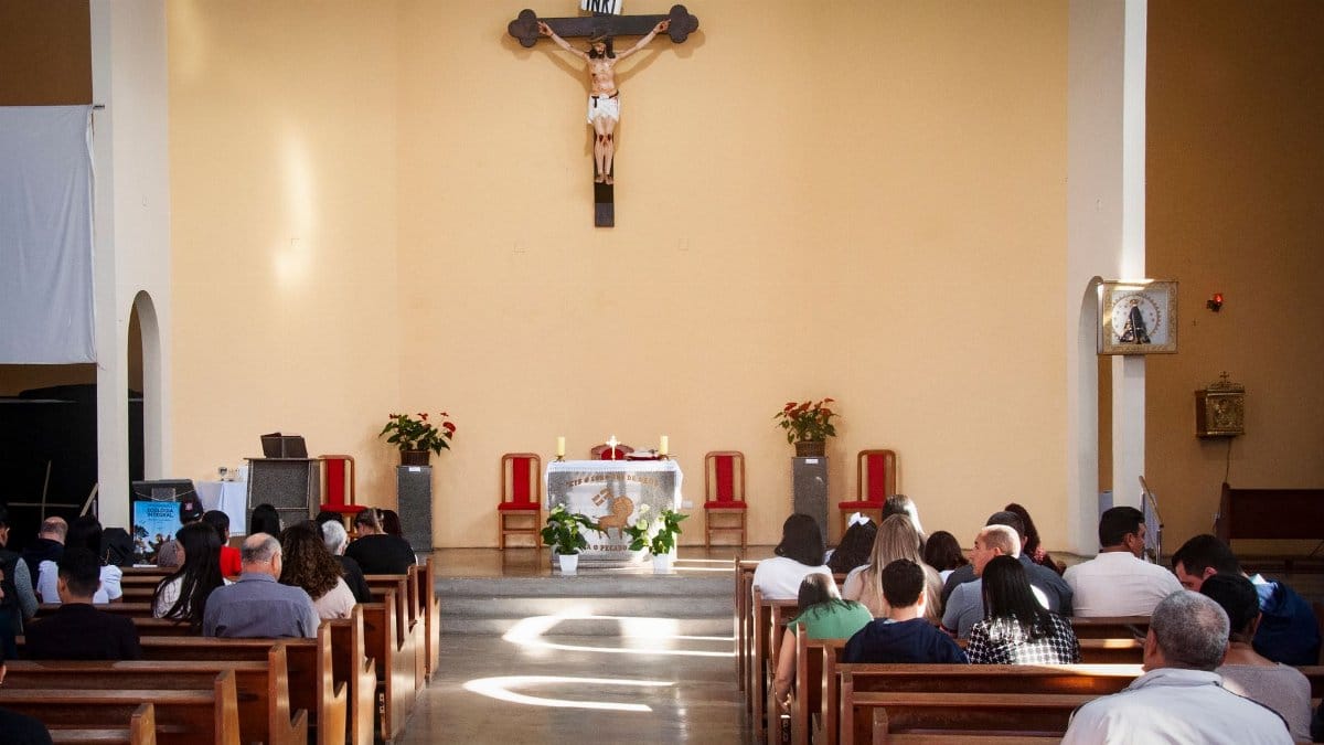 An interior view of a church with a congregation attending a religious service with a prominent crucifix.