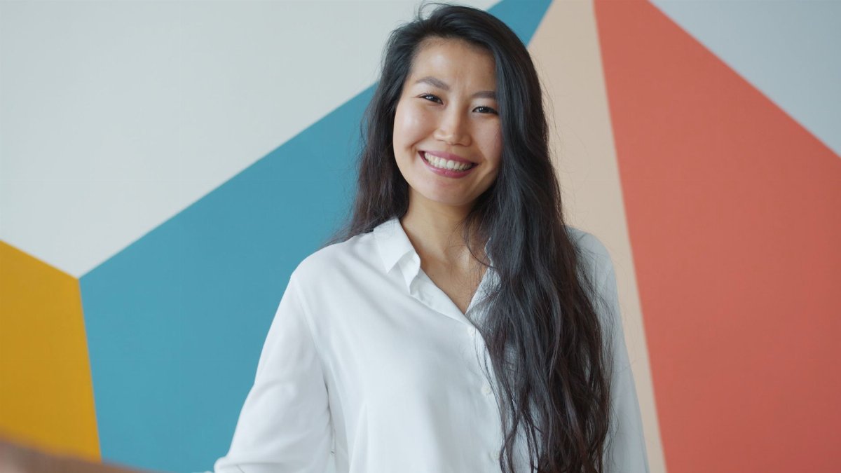 Smiling woman in white shirt standing before colorful geometric wall art, exuding warmth.