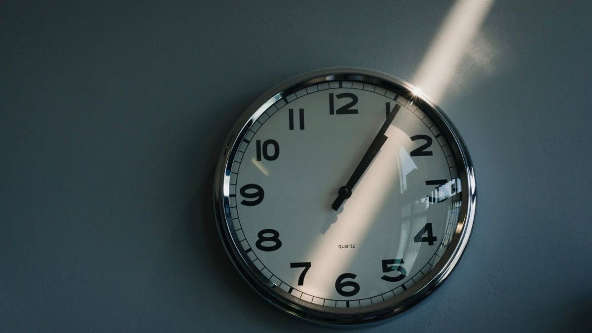 Close-up of a round wall clock illuminated by sunlight indoors, reflecting time passage.