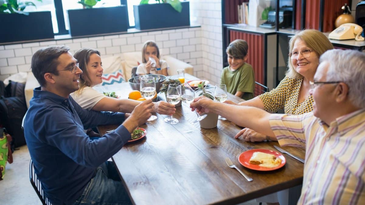 A joyful family gathering around a table, toasting with drinks and enjoying a meal indoors.