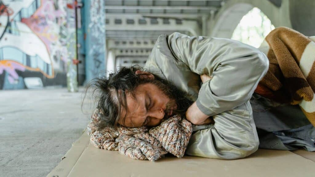 A homeless man sleeping on cardboard under a bridge, highlighting urban poverty.