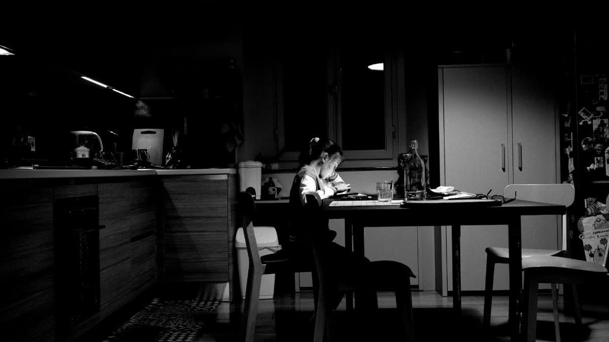 A child studying alone at a dimly lit kitchen table, creating a moody atmosphere.