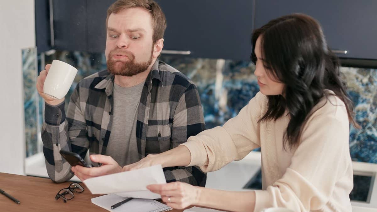 A couple looks worried as they review bills at their kitchen table, reflecting financial concerns.