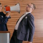 Dynamic image of two politicians arguing; one shouts into a megaphone in a heated debate.