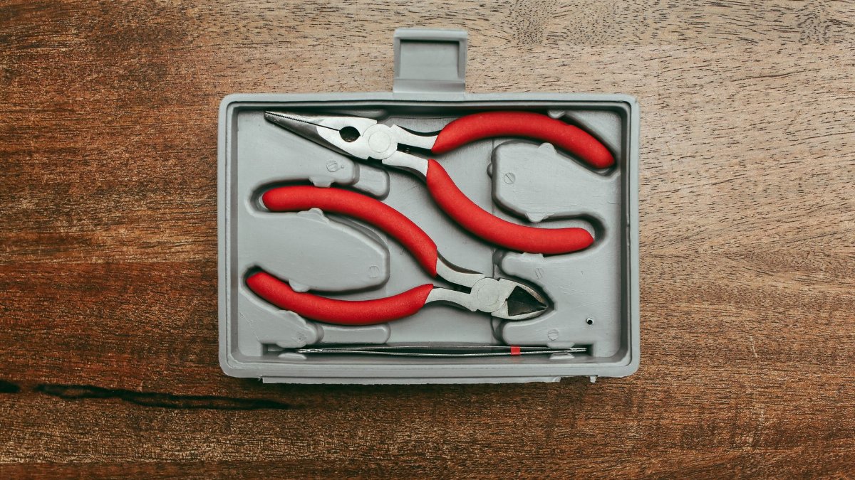 Top view of a red handled pliers set in a box on a wooden surface.