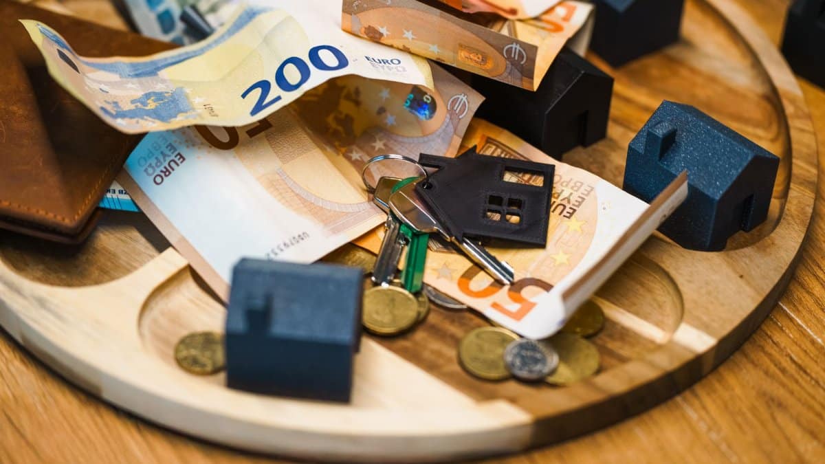 Euro currency, keys, and miniature houses symbolize real estate and finance concepts.