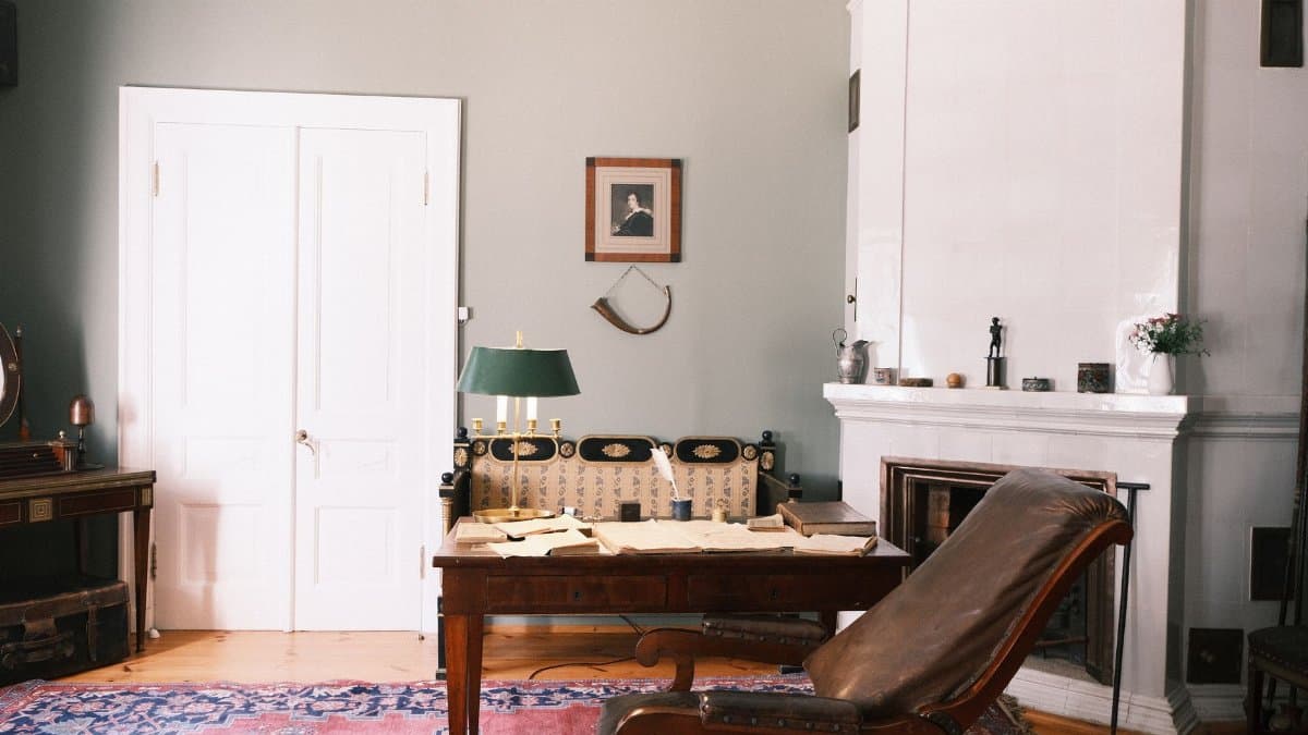 A cozy vintage study room featuring a leather armchair, fireplace, wooden desk, and classic decor elements.