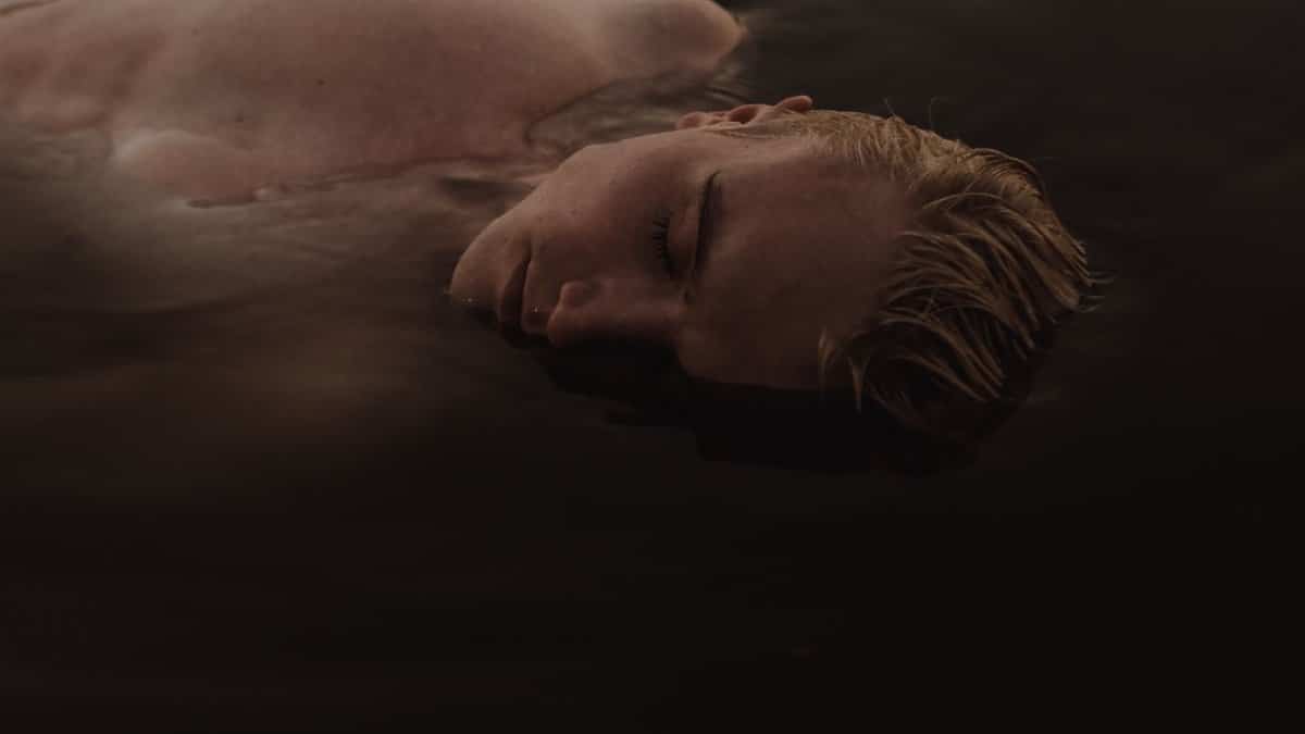 A serene moment as a topless man floats peacefully on still water with closed eyes.