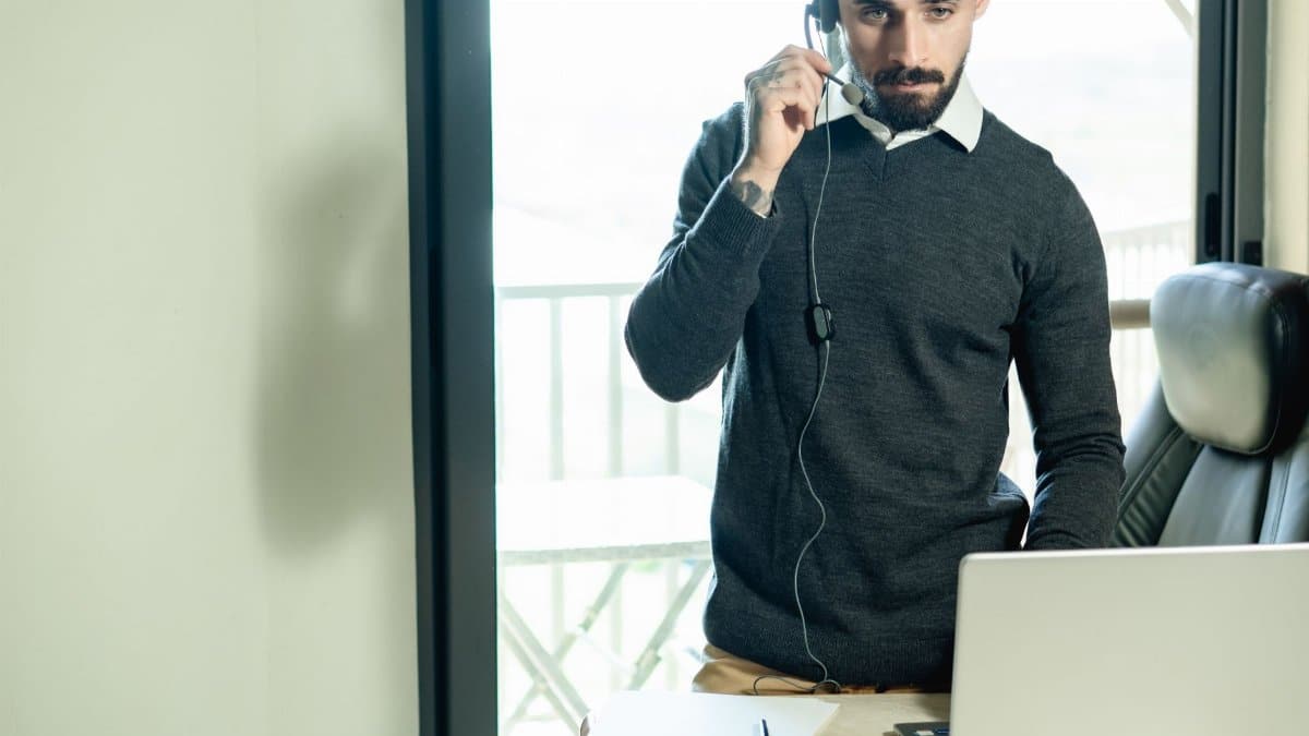 A man in an office with a headset providing customer service from a laptop.