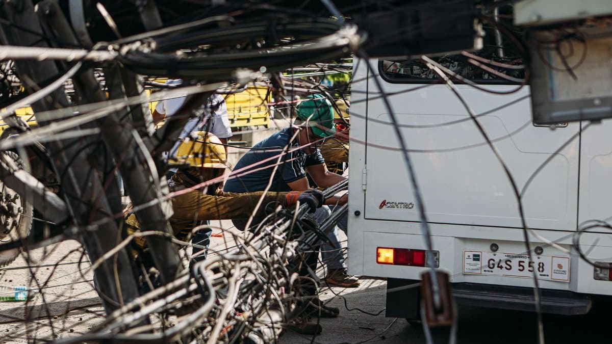 Technicians working on tangled overhead wires next to a vehicle on a sunny day.