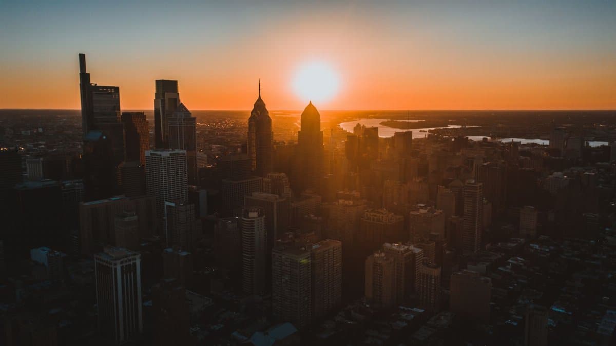 Aerial view of high building facades near ocean illuminated by glowing sun in colorful sky at sunset