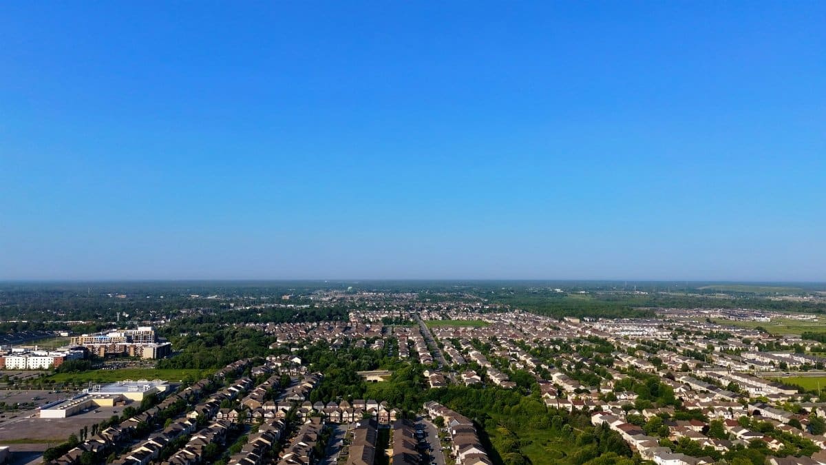 Aerial panorama of suburban community with clear blue skies, showing houses and green spaces.
