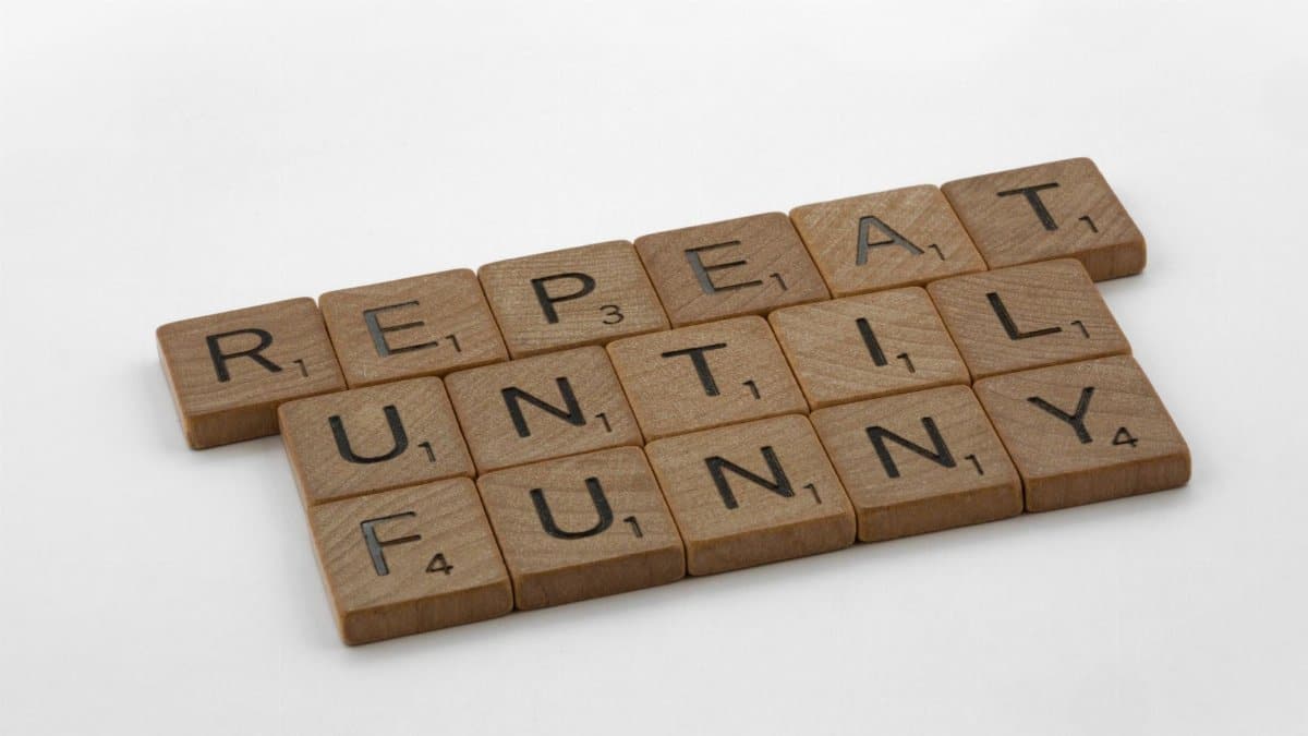 Wooden Scrabble tiles spelling 'repeat until funny' on a white background, conveying humor.
