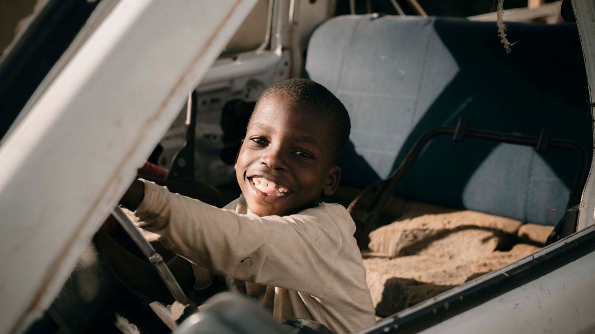 A smiling child sits inside an old car, capturing a moment of joy and playfulness.