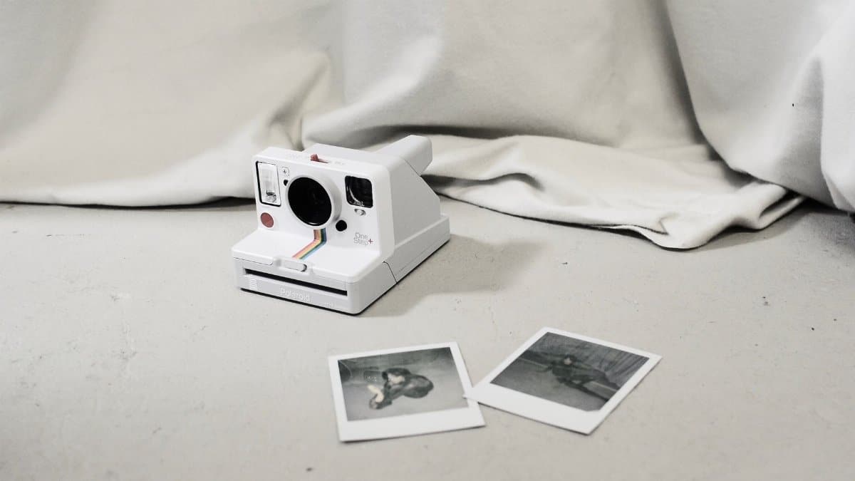 Modern instant photo camera and instant photos placed on floor near light curtain