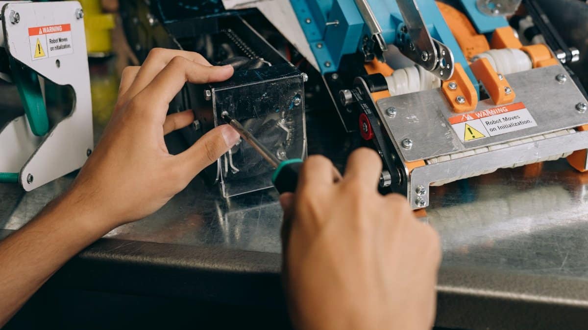 Hands of a technician repairing robotic machinery with precision tools on a workbench.