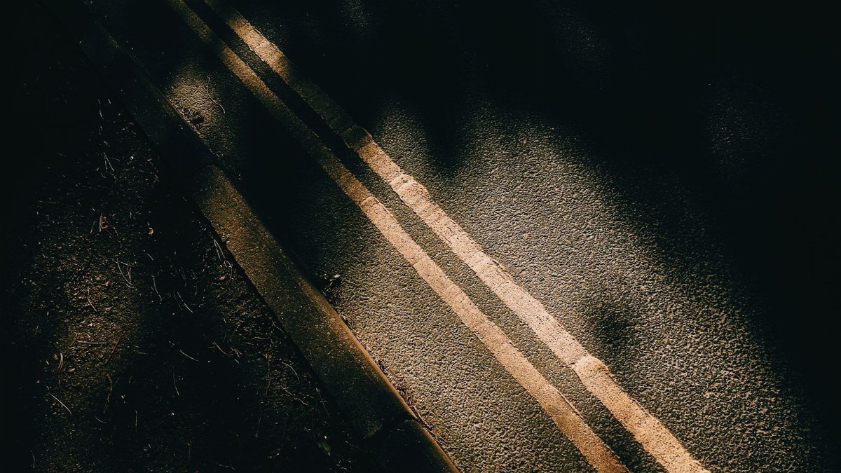 From above of asphalt roadway with yellow marking lines with dark shades near ground in sunny day in street