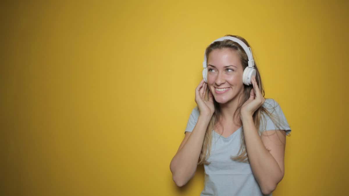 Smiling woman listening to music on headphones against a sunny yellow background.