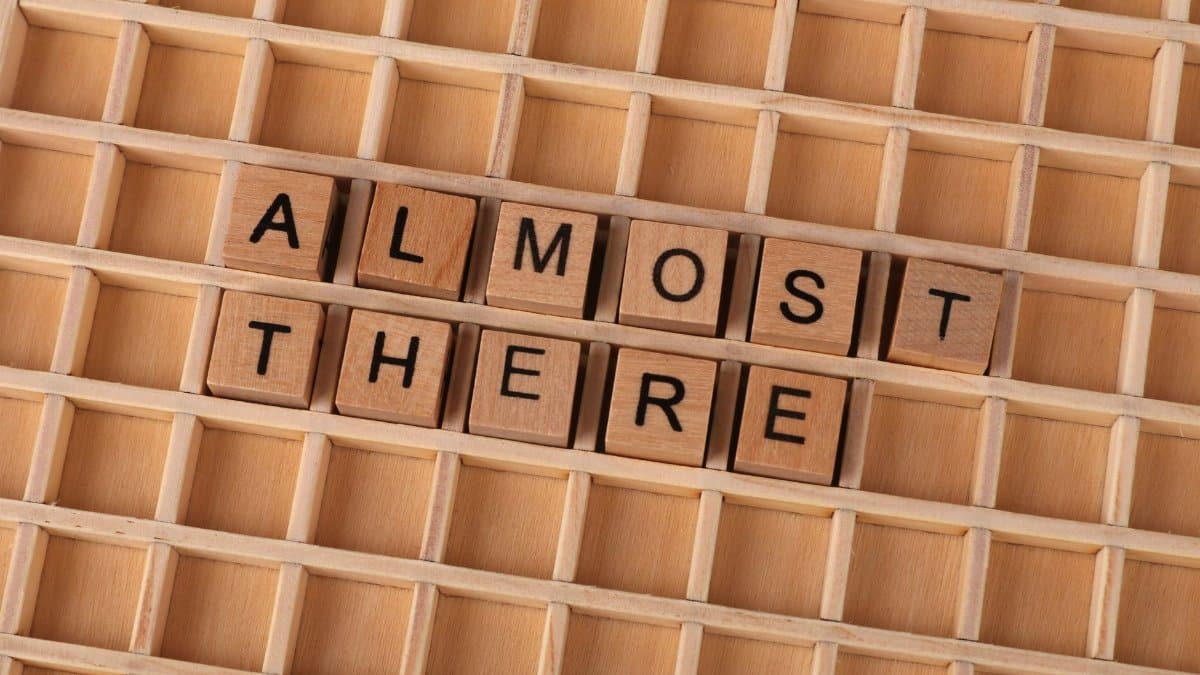 Wooden Scrabble tiles spelling 'Almost There' on a wooden game board, motivational concept.