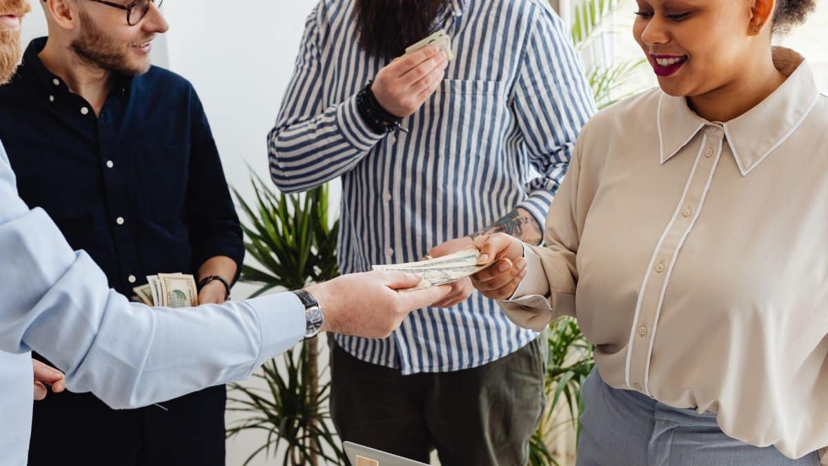Business professionals exchanging money in a casual office setting.