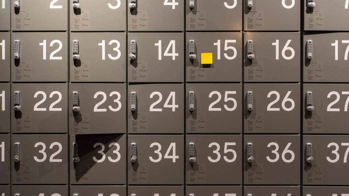 Gray lockers with electronic locks featuring numbers and a single yellow sticky note in the center.