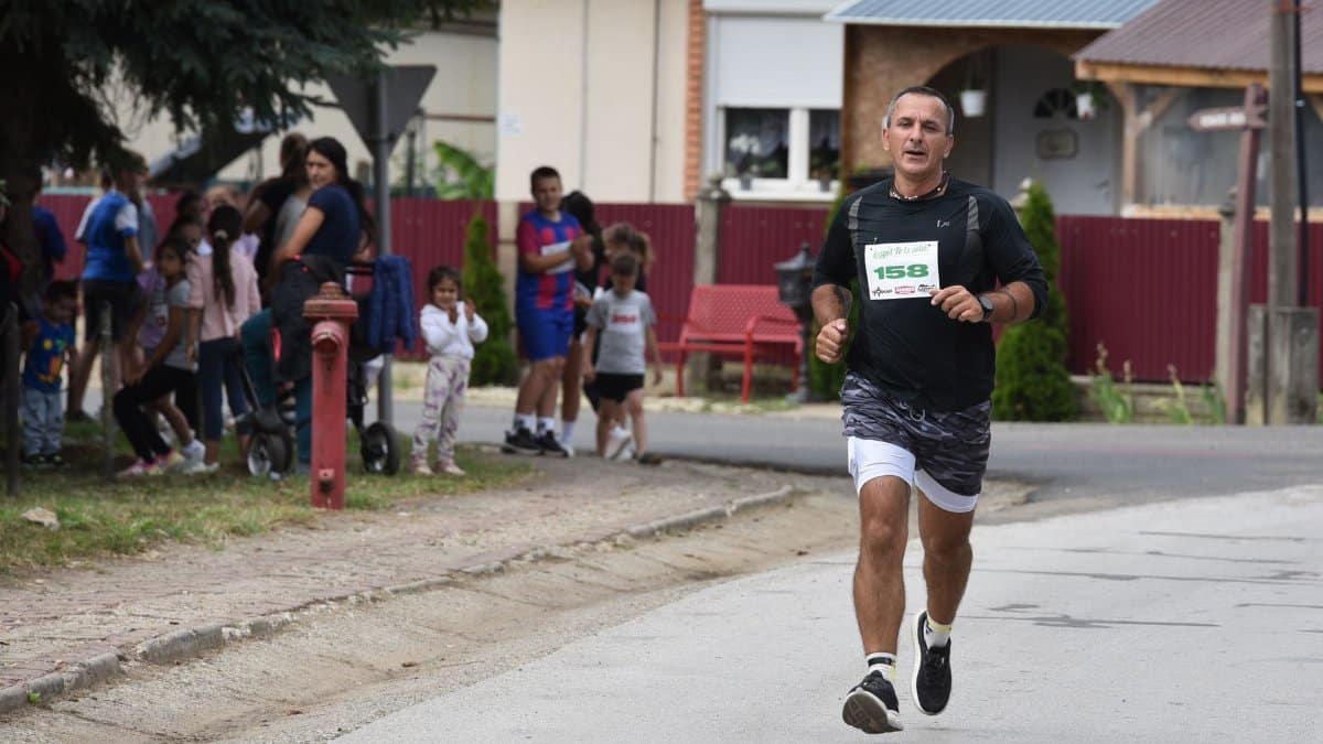 Athlete running in suburban marathon with spectators watching from sidewalk.