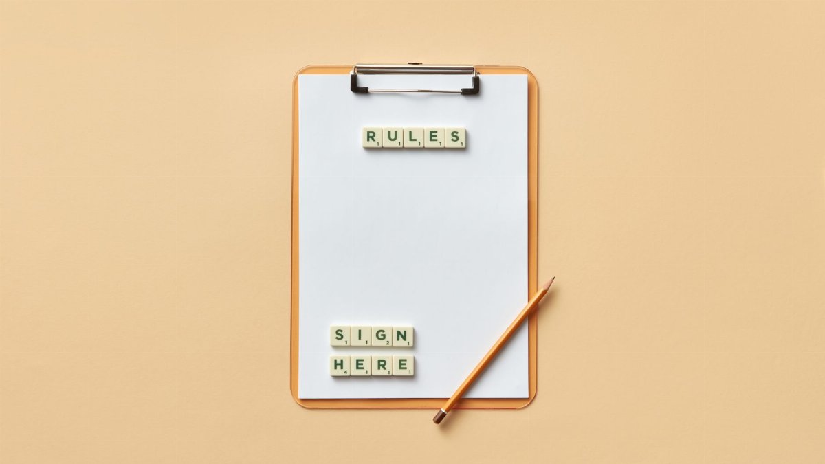 Flat lay of clipboard with letter tiles spelling 'rules' and 'sign here', accompanied by pencil on beige background.