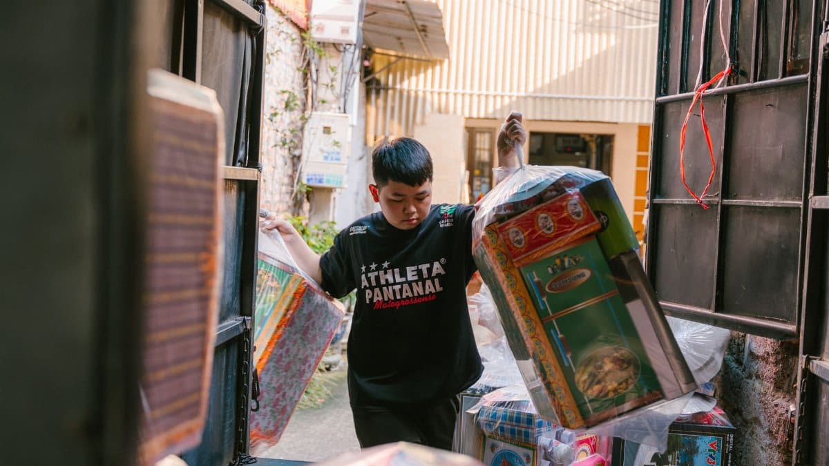 A young boy unloading packages from a truck outdoors during the day.