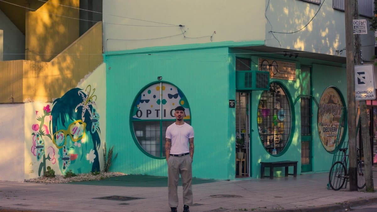 A man stands in front of a vibrant mural on a sunny street in Argentina.