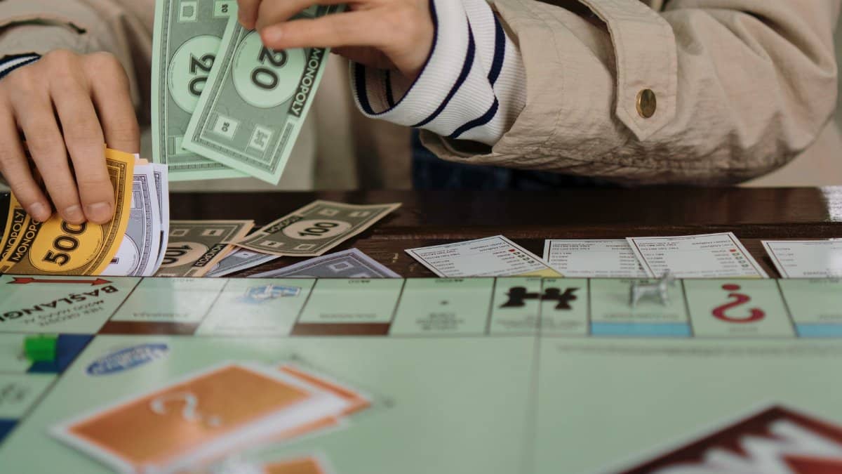Hands counting Monopoly money during a board game session, highlighting fun and strategy.