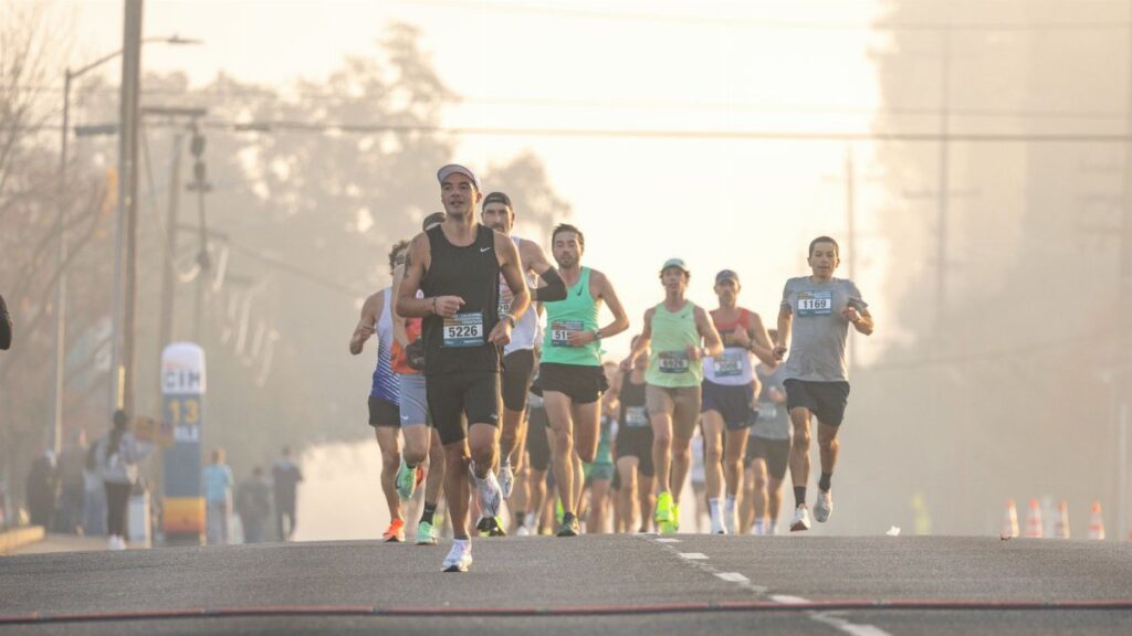 Group of runners in a marathon race on a foggy morning street with trees in the background.