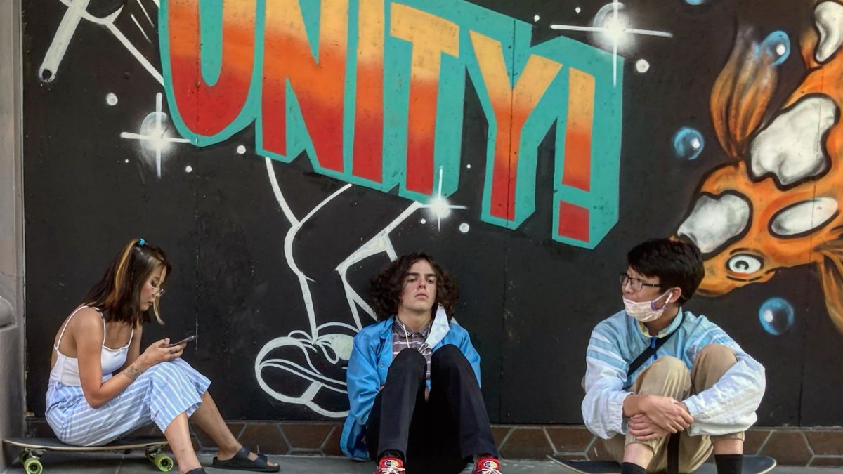 Teens sitting with skateboards in front of a vibrant 'Unity' graffiti mural in San Diego.