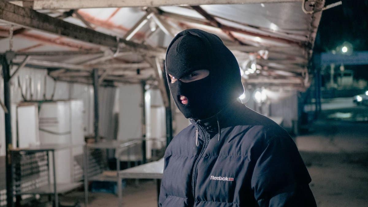 A person in a balaclava and jacket standing at an empty night market, creating a mysterious mood.