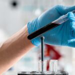 Close-up of a gloved hand holding a test tube with blood sample in a clinical research lab.