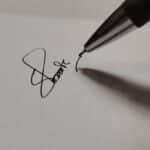 Macro shot of a pen writing a signature on white paper, emphasizing precision.