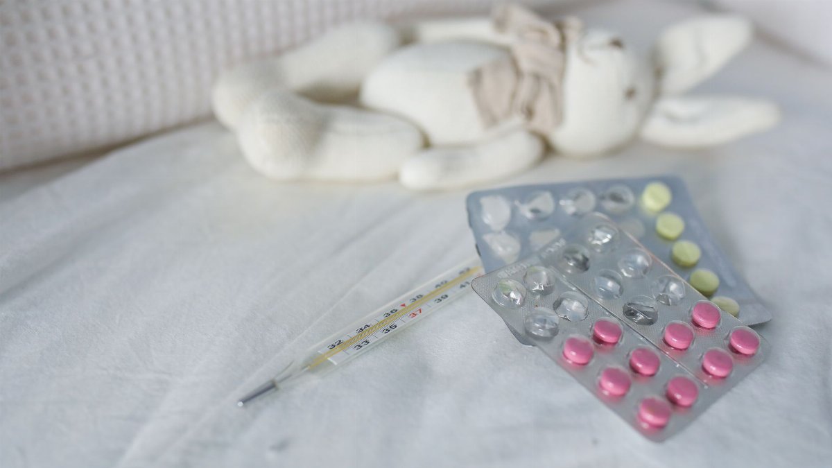 Close-up of medication and thermometer on a bed beside a plush rabbit toy, symbolizing childhood illness care.